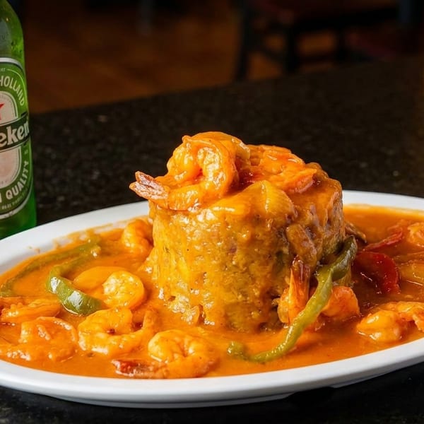 Mofongo with shrimp in a rich orange sauce, green peppers, and a Heineken bottle.