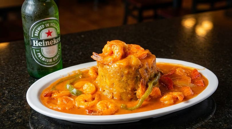 Mofongo with shrimp in a rich orange sauce, green peppers, and a Heineken bottle.