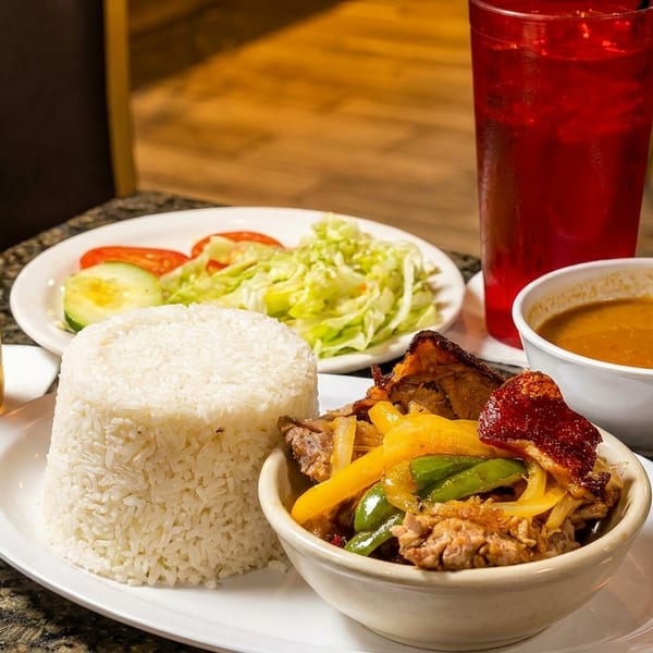 A Modelo beer, rice, meat with peppers, salad, soup, and a red drink on a table.